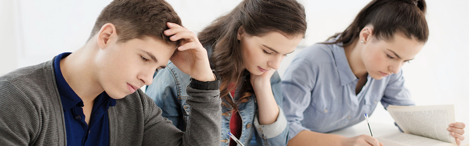 Three students sitting next to each other at a table each looking at a textbook
