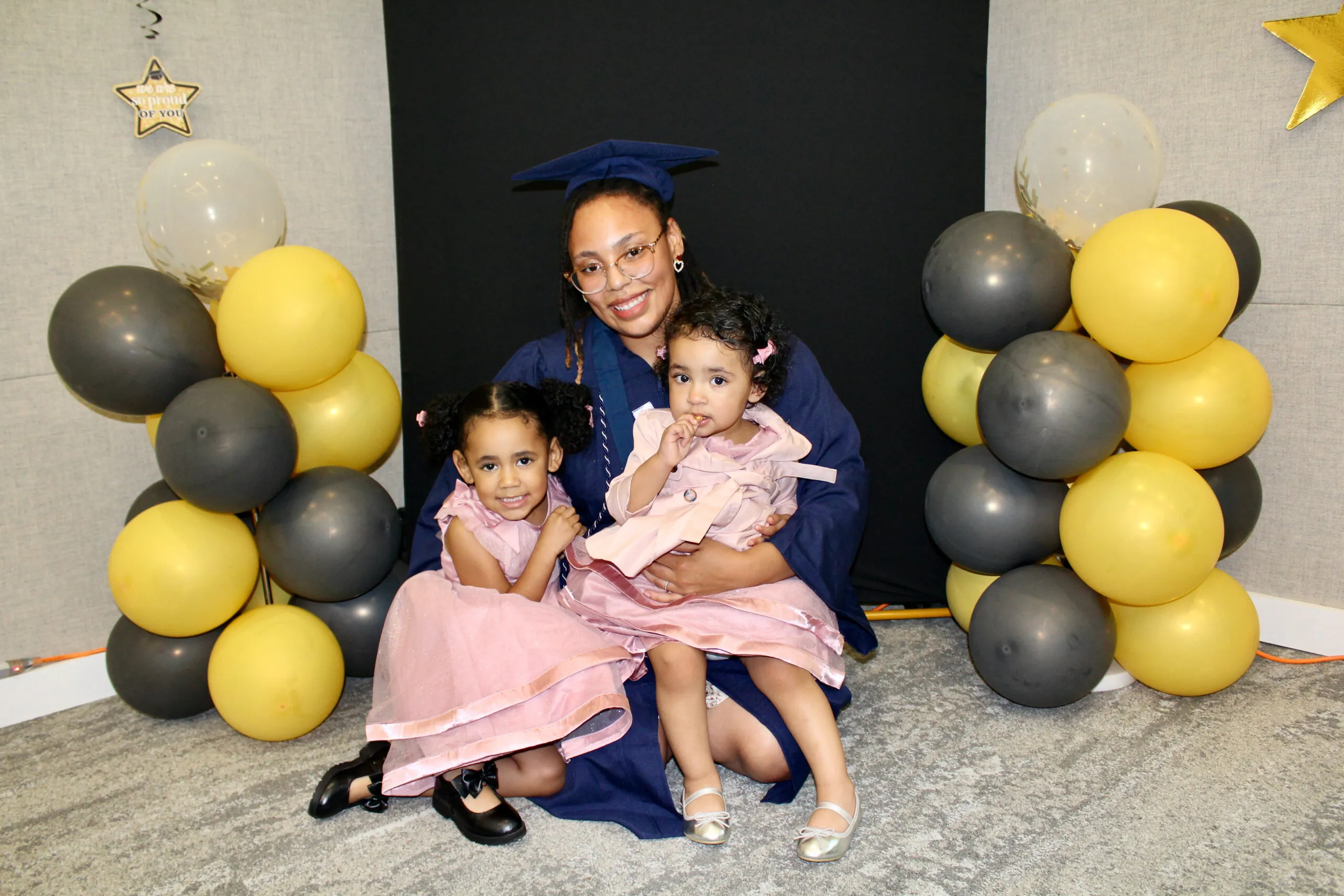 student in cap & gown posing with her two daughters