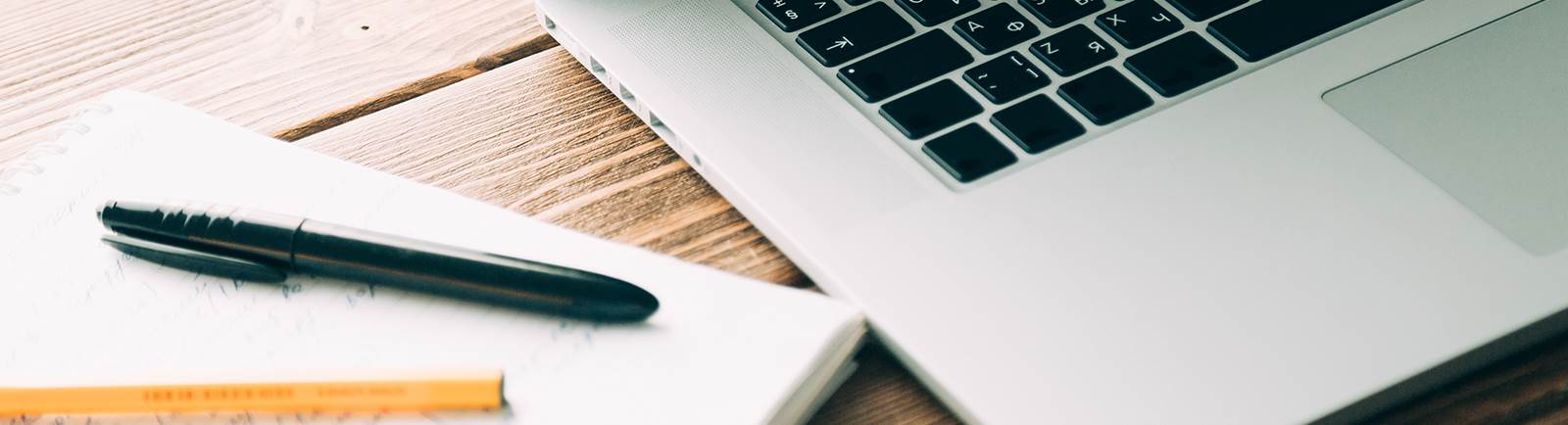 close up of a pad of paper, pens and laptop