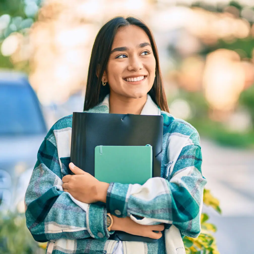 A smiling college student carrying a notebook.