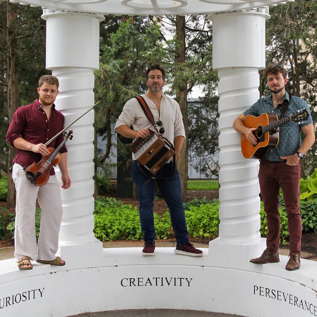 Three men with musical instruments stand on a circular white structure with spiral columns.