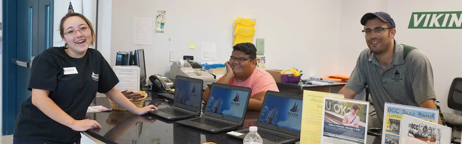 three students at computers smiling at the camera