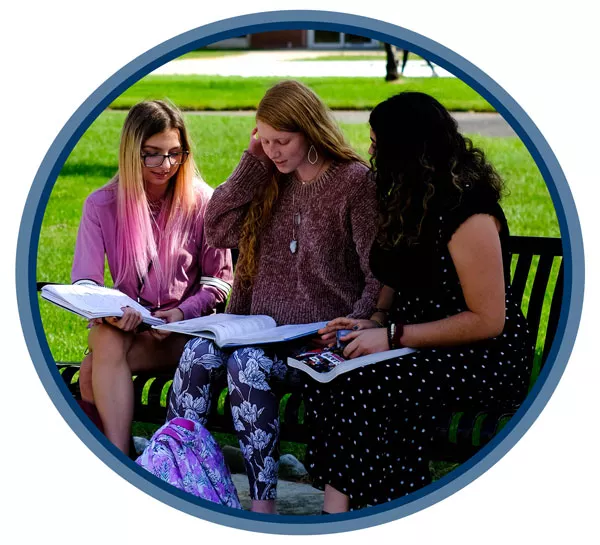 three students sitting on a bench on campus studying